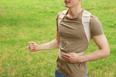 Closeup view of man with orthopedic corset on green grass outdoors, space for text