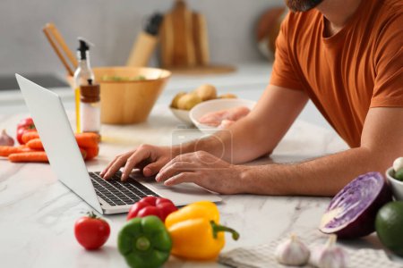 Photo for Man making dinner while watching online cooking course via laptop in kitchen, closeup - Royalty Free Image