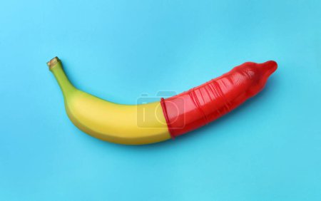 Téléchargez les photos : Banane avec préservatif sur fond bleu clair, vue de dessus. Concept de sexe sûr - en image libre de droit