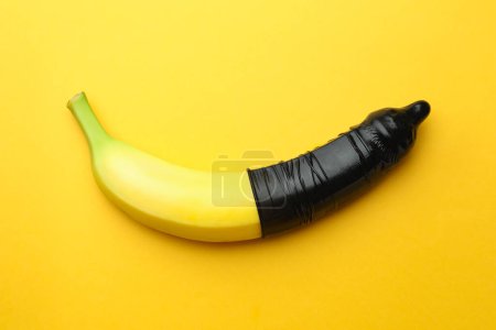 Téléchargez les photos : Banane avec préservatif sur fond orange, vue de dessus. Concept de sexe sûr - en image libre de droit