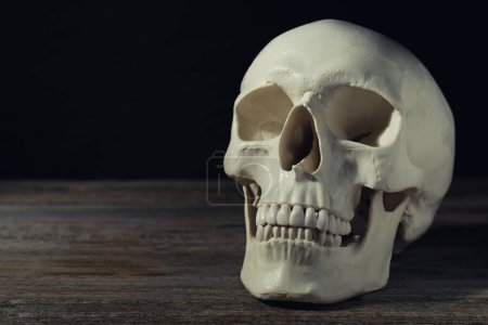 Photo for Human skull on wooden table against black background, space for text - Royalty Free Image