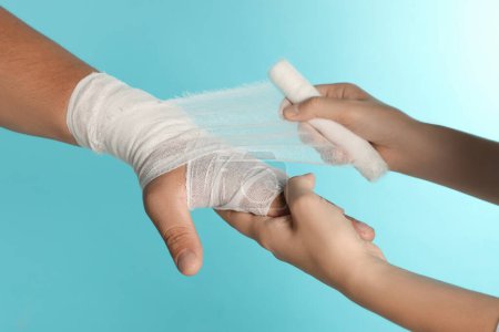 Foto de Médico aplicando vendaje en la mano del paciente sobre fondo azul claro, primer plano - Imagen libre de derechos