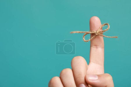 Foto de Hombre mostrando el dedo índice con lazo atado como recordatorio sobre fondo turquesa, primer plano. Espacio para texto - Imagen libre de derechos