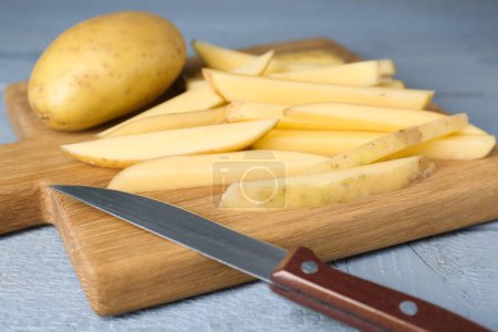 Téléchargez les photos : Pommes de terre entières et coupées au couteau sur une table en bois gris, gros plan. Cuisiner de délicieuses frites - en image libre de droit
