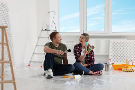 Photo for Happy couple with brushes and painting tools on floor in apartment during repair - Royalty Free Image