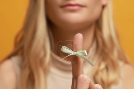Photo for Woman showing index finger with tied bow as reminder against orange background, focus on hand - Royalty Free Image