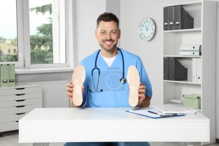 Handsome male orthopedist showing insoles in hospital