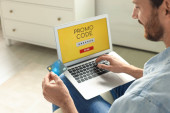 Man holding laptop with activated promo code and credit card indoors, closeup Poster #624635978