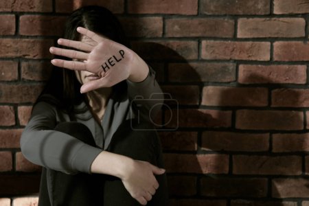 Foto de Concepto de violencia doméstica. Mujer escondiendo su cara, concéntrate en la mano con la palabra escrita Help - Imagen libre de derechos