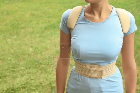 Photo for Closeup view of woman with orthopedic corset on green grass outdoors, space for text - Royalty Free Image