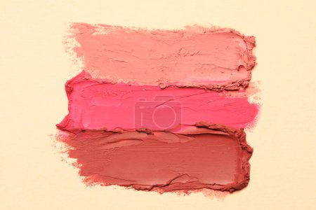 Smears of beautiful lipsticks on beige background, top view
