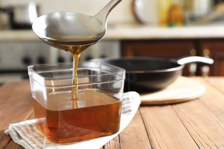 Téléchargez les photos : Verser l'huile de cuisson usagée avec louche dans un récipient sur une table en bois dans la cuisine - en image libre de droit
