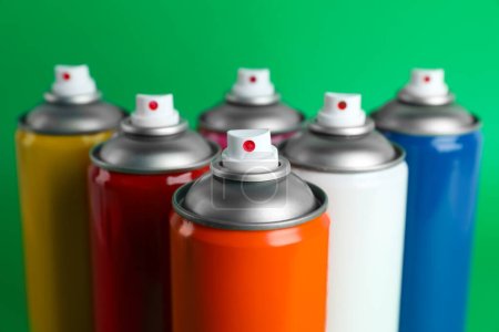 Colorful cans of spray paints on green background, closeup