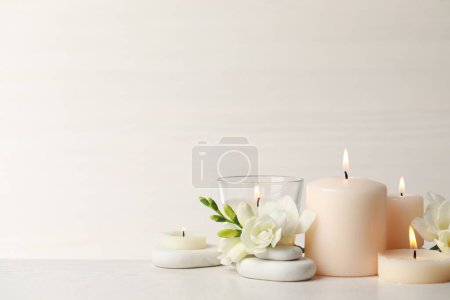 Foto de Hermosa composición con velas encendidas, piedras de spa y flores en la mesa blanca. Espacio para texto - Imagen libre de derechos