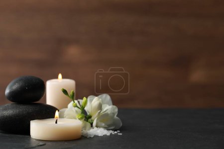 Téléchargez les photos : Belle composition avec des pierres de spa, des bougies allumées et des fleurs sur table noire. Espace pour le texte - en image libre de droit