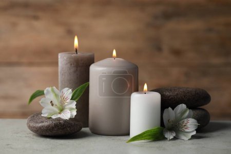 Photo for Beautiful composition with burning candles, spa stones and flowers on light grey table - Royalty Free Image
