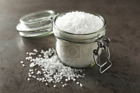 Glass jar of natural sea salt on grey table