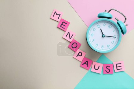 Pink paper notes with word Menopause and alarm clock on color background, flat lay. Space for text