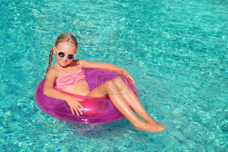 Téléchargez les photos : Petite fille mignonne avec anneau gonflable dans la piscine le jour ensoleillé. espace pour le texte - en image libre de droit
