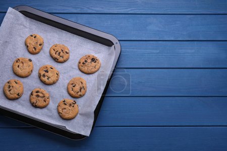 Téléchargez les photos : Plat à pâtisserie avec biscuits et papier parchemin sur table en bois bleu, vue sur le dessus. Espace pour le texte - en image libre de droit
