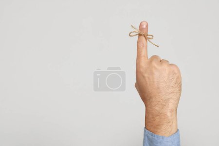 Photo for Man showing index finger with tied bow as reminder on light grey background, closeup. Space for text - Royalty Free Image
