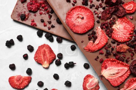 Chocolate bars with freeze dried berries on grey marble table, flat lay