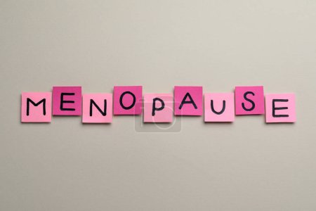 Notes en papier rose avec mot Ménopause sur fond beige, pose plate