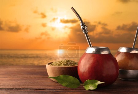 Foto per Calabash con mate tea e bombilla sul tavolo in legno all'aperto al tramonto. Spazio per testo - Immagine Royalty Free