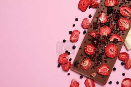 Barre de chocolat avec fruits lyophilisés sur fond rose, plat. Espace pour le texte