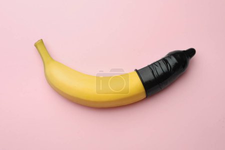 Téléchargez les photos : Banane avec préservatif sur fond rose, vue de dessus. Concept de sexe sûr - en image libre de droit