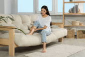 Young woman rubbing sore leg on sofa at home Poster #625062090