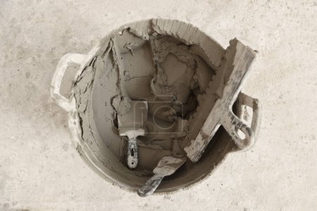 Photo for Bucket with cement and putty knifes on floor, top view - Royalty Free Image