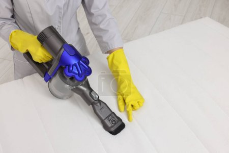 Photo for Woman in gloves disinfecting mattress with vacuum cleaner indoors, closeup. Space for text - Royalty Free Image