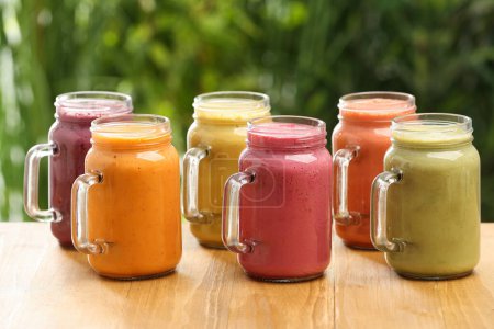 Photo for Many different delicious smoothies in mason jars on wooden table against blurred background - Royalty Free Image