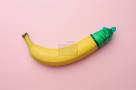 Téléchargez les photos : Banane avec préservatif sur fond rose, vue de dessus. Concept de sexe sûr - en image libre de droit