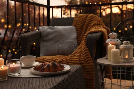 Hermosa vista de muebles de jardín con almohada, manta suave y velas encendidas en el balcón