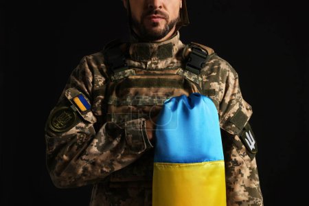 Soldat in Militäruniform mit ukrainischer Flagge auf schwarzem Hintergrund, Nahaufnahme