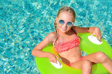 Téléchargez les photos : Petite fille mignonne avec des lunettes de soleil et anneau gonflable dans la piscine le jour ensoleillé - en image libre de droit
