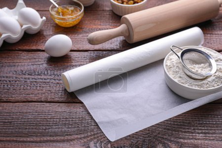 Téléchargez les photos : Rouleau de papier sulfurisé et d'ingrédients sur table en bois - en image libre de droit
