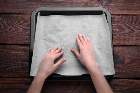 Téléchargez les photos : Femme mettant du papier parchemin dans une casserole à table en bois - en image libre de droit