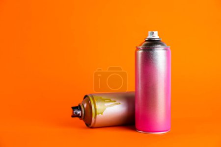 Foto de Latas usadas de pintura en spray sobre fondo naranja. Espacio para texto - Imagen libre de derechos