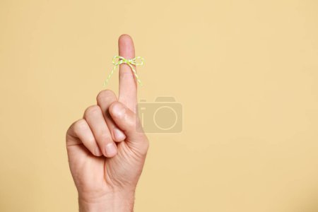 Photo for Man showing index finger with tied bow as reminder on beige background, closeup. Space for text - Royalty Free Image