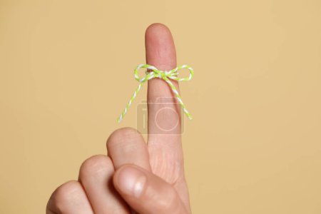 Photo for Man showing index finger with tied bow as reminder on beige background, closeup - Royalty Free Image