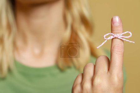 Photo for Woman showing index finger with tied bow as reminder against light brown background, focus on hand - Royalty Free Image