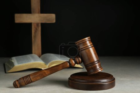 Judge gavel, bible and wooden cross on light grey table against black background