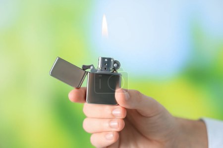 Foto de Hombre sosteniendo encendedor con llama ardiente contra fondo verde borroso, primer plano - Imagen libre de derechos