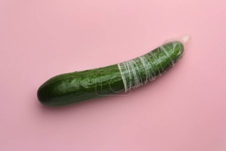 Téléchargez les photos : Concombre avec préservatif sur fond rose, vue de dessus. Concept de sexe sûr - en image libre de droit