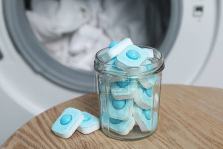 Photo for Jar with water softener tablets on wooden table near washing machine - Royalty Free Image
