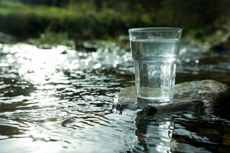 Foto de Un vaso de agua dulce en piedra cerca del río al aire libre. Espacio para texto - Imagen libre de derechos