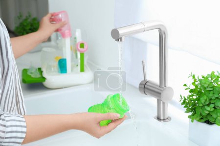 Photo for Woman washing baby bottle under stream of water in kitchen, closeup - Royalty Free Image